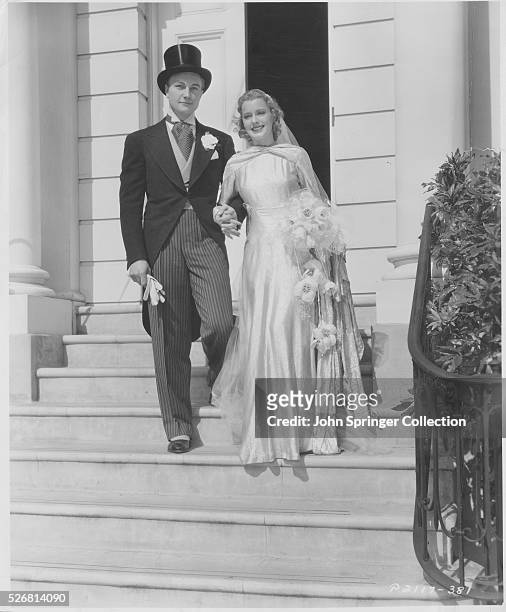 Actor Richard Denning and actress Ellen Drew model fashionable 1930's wedding attire as as they pose as bride and groom.