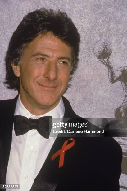 American actor Dustin Hoffman poses in a tuxedo at a formal event, mid 1990s. He wears a red AIDS awareness ribbon on his lapel.