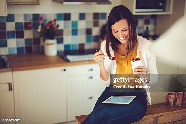 hispanic woman reading tablet and having breakfast in the kitchen - women yogurt stock pictures, royalty-free photos & images