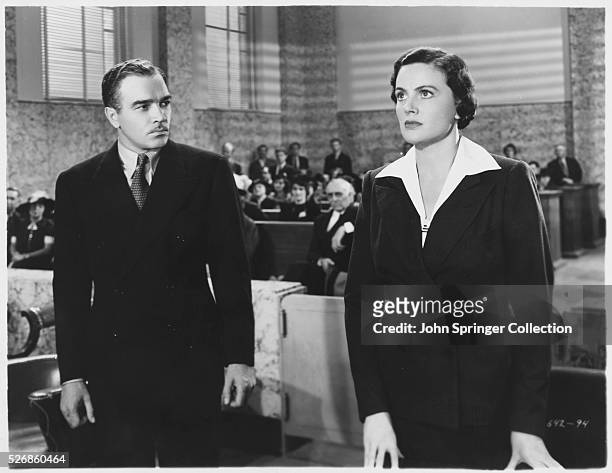 Walter Abel watches Frieda Inescort while they stand before the judge in the 1937 film Portia on Trial.