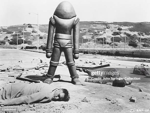 An alien stands among corpses and depris in a scene from the 1956 film Earth vs. The Flying Saucers.