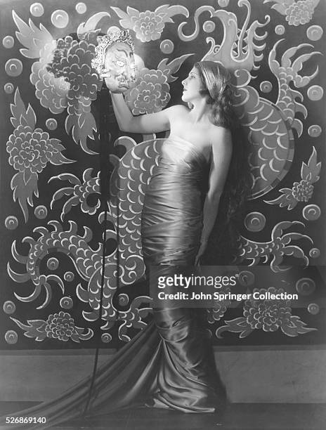 Portrait of actress Jean Arthur holding an asian style mask.