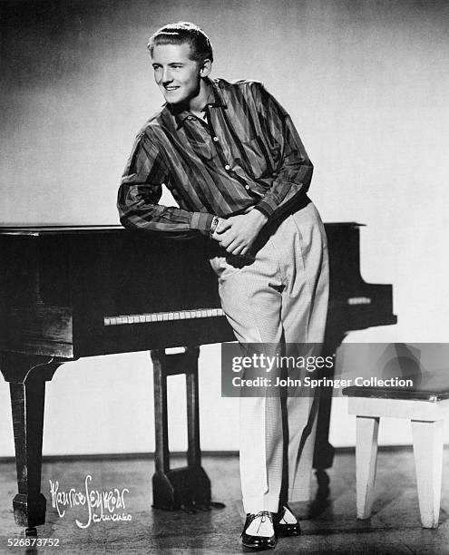 Portrait of pianist and singer Jerry Lee Lewis leaning on a piano.