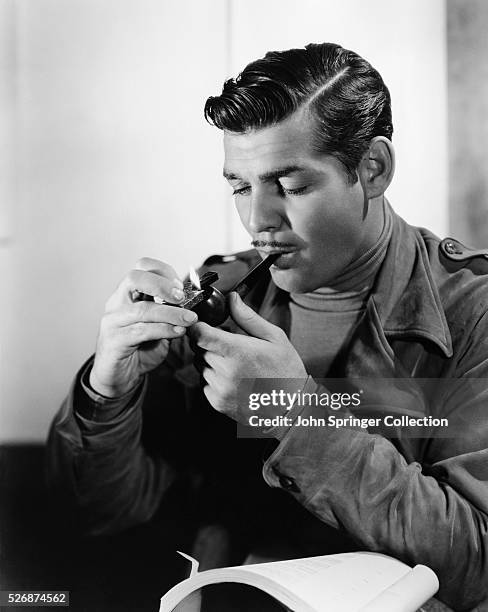 Clark Gable lights his pipe while reading over the script for San Francisco, a romantic drama directed by W.S. Van Dyke.