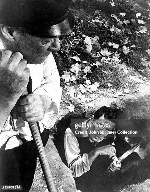 Captain Albert Wiles stands above Sam Marlowe in a scene from Alfred Hitchcock's 1955 film, The Trouble with Harry.