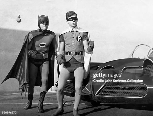 Adam West as Batman and Burt Ward as Robin in the original 1966 television series Batman standing near the Batmobile convertible.