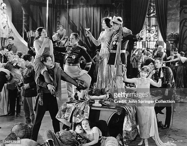Celebratory scene from the 1924 film Three Weeks features John Sainpolis as The King and Claire de Lorez as Mitz, both of whom are standing on the...