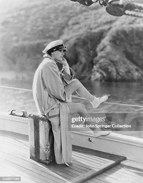 GRETA GARBO UNDATED PHOTO GARBO LOOKS PENSIVE WEARING A CAPTAIN'S HAT WHILE SITTING ON A BOX ON THE DECK OF A SHIP.