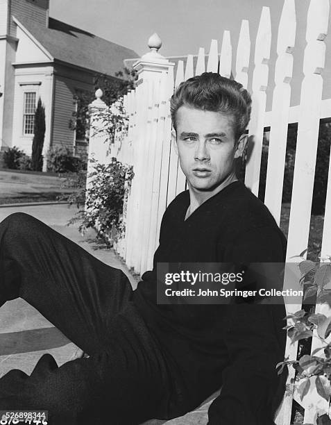 Cal Trask sits on the ground leaning on a picket fence in a publicity still for East of Eden.