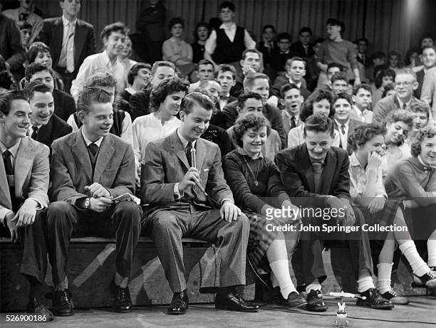 Mpene from Dick Clark's "American Bandstand," in which Clark sits in the audience with his teenage audience to watch a toy on the ground before them....