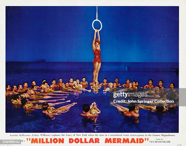 Esther Williams, portraying Australian swimmer Annette Kellerman, hangs from a ring above a circle of synchronized swimmers.