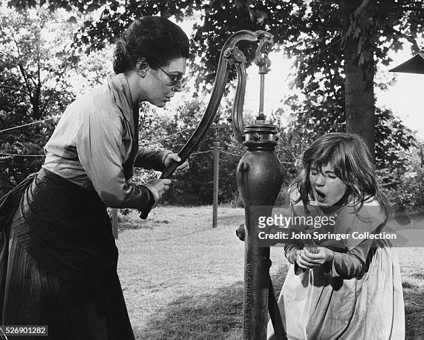 Young Helen Keller and her teacher Anne Sullivan go to fill a bucket at the water pump. As the water pours over her hand, Helen suddenly realizes...