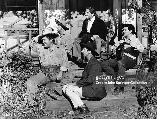 The cast of Tortilla Flat sitting on a porch during a scene: Spencer Tracy as Pilon, John Garfield as Danny, Akim Tamiroff as Pablo, John Qualen as...