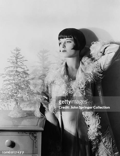 Silent film star, Louise Brooks , standing 3/4 length next to a small decorative tree. Photograph circa 1920s.