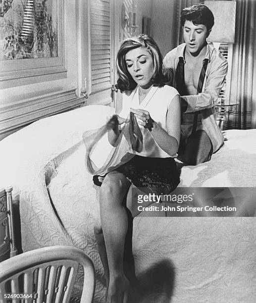 Benjamin Braddock unbuttons the back of Mrs. Robinson's blouse in the bedroom during a scene from Mike Nichols' 1967 comedic romance The Graduate.