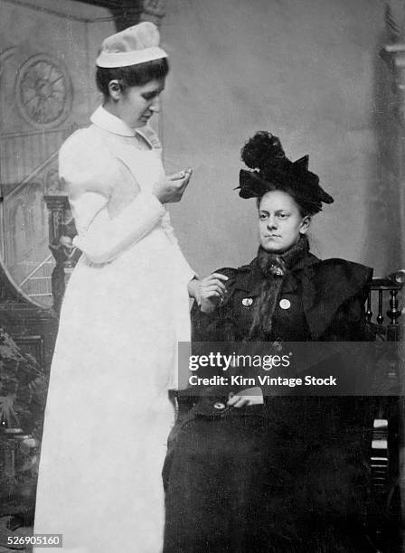 Wealthy late-Victorian era woman with a thermometer in her mouth has her heartbeat checked by a nurse in a tintype portrait.