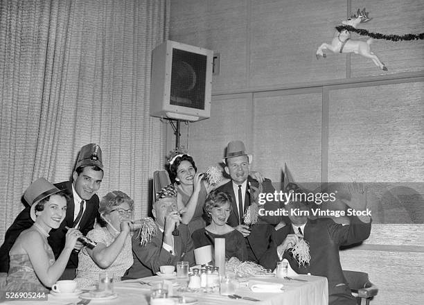 Party hats and noise makers adorn party goers at a holiday party group at the American mid-century.