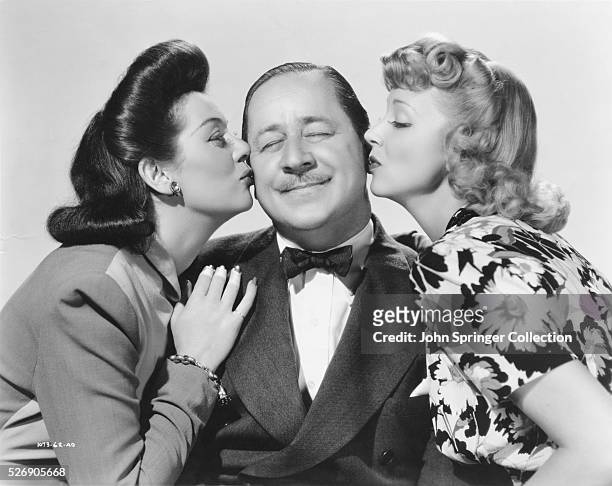 Content Robert Benchley receives kisses from Rosalind Russell and Virginia Bruce in the 1940 comedy Hired Wife, in which, the trio play the...