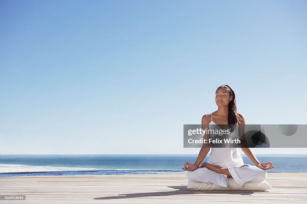 Woman meditating on deck near ocean