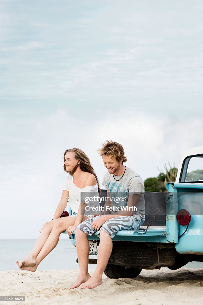 Couple sitting on tailgate of truck on beach