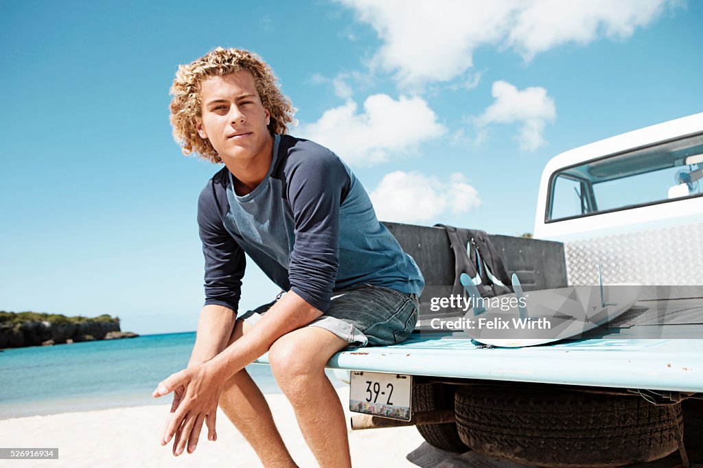 Young man sitting on trailer with surfboard