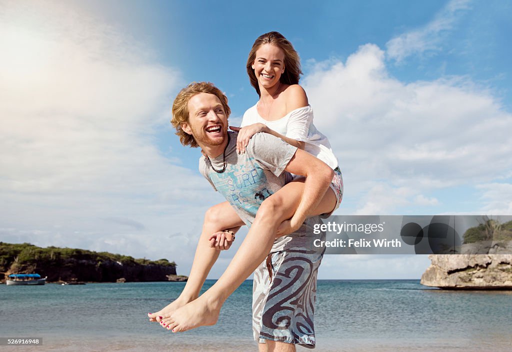 Young man giving woman piggyback ride on beach