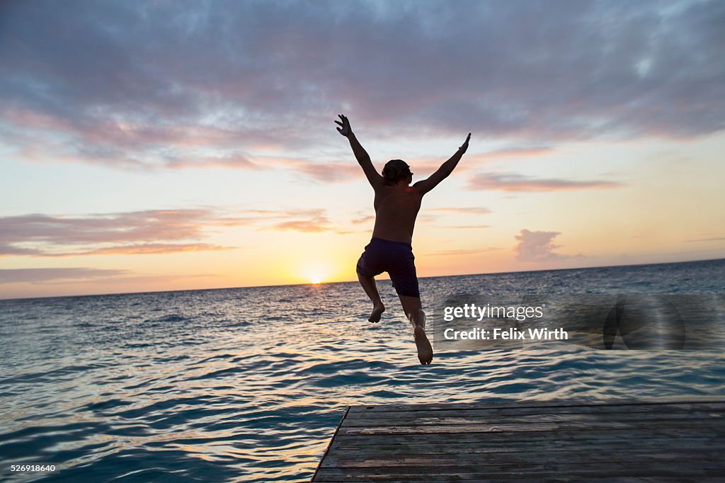 Young man jumping into water at sunset