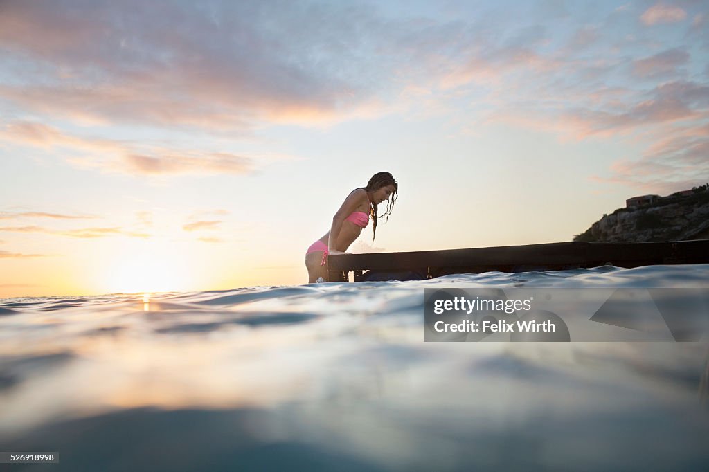 Young woman ascending wooden pier at sunset
