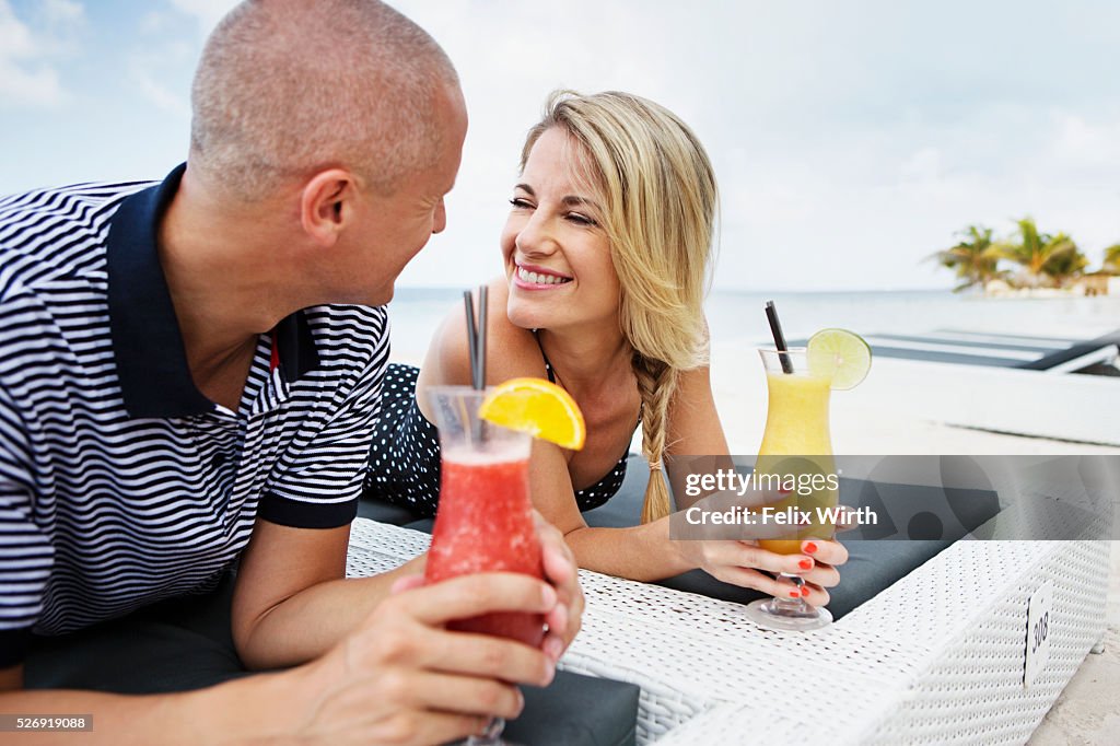 Portrait of couple having drink on deck chair on beach