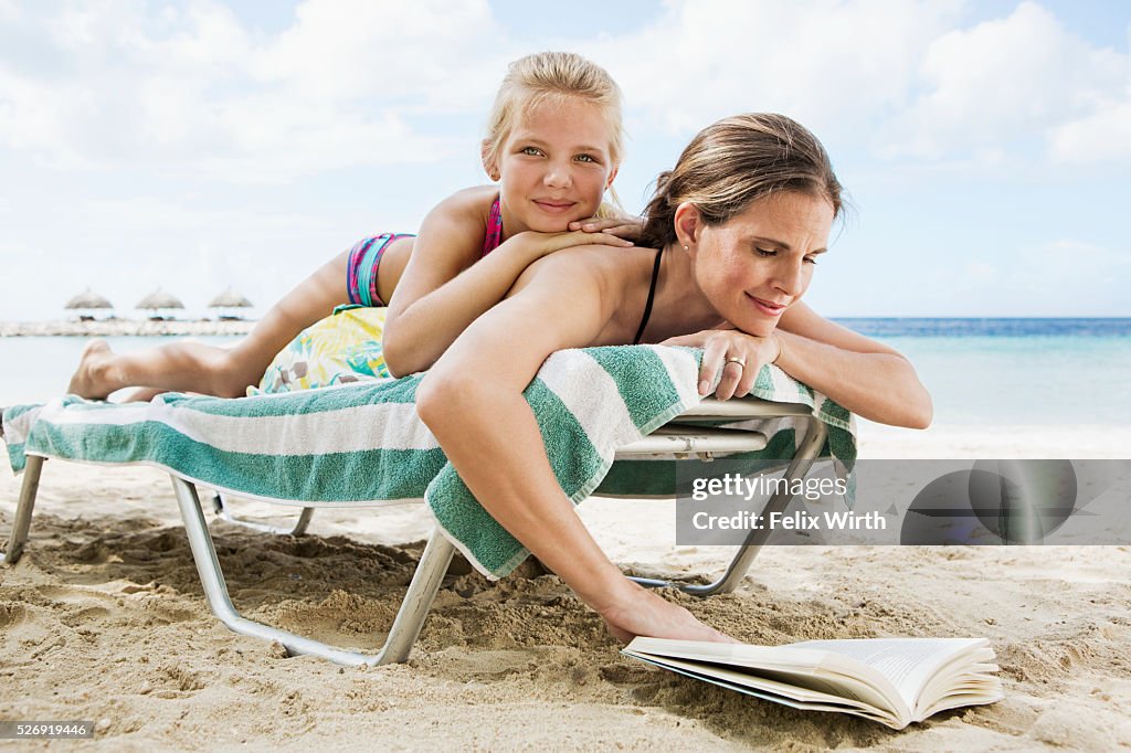 Mother with daughter (10-12) relaxing on deckchair on beach