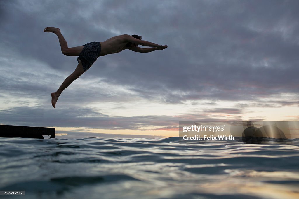 Young man jumping into water at sunset