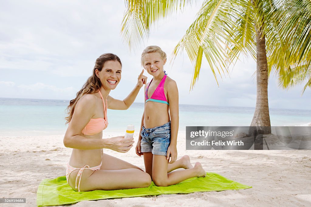 Mother and daughter (10-12) using tanning lotion on beach