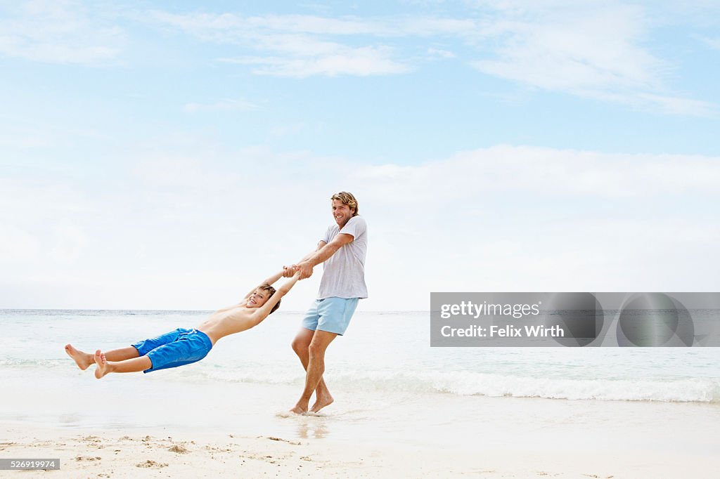 Father spinning his son (10-12) in air on beach