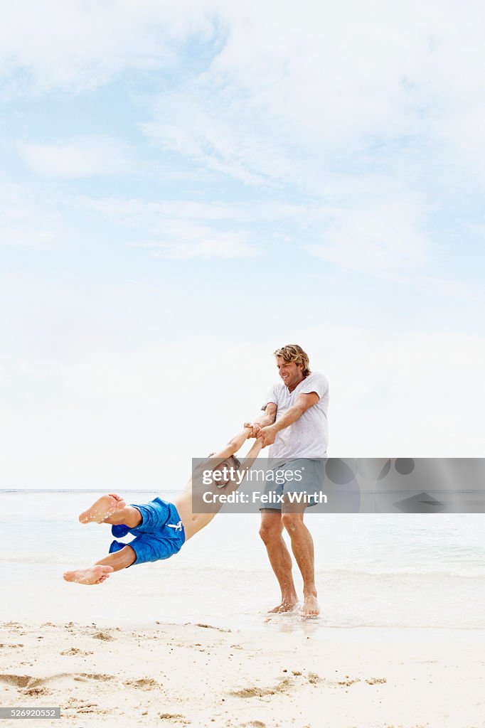 Father spinning his son (10-12) in air on beach