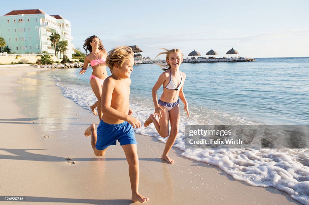 Mother with son (8-9) and daughter (10-11) running on beach