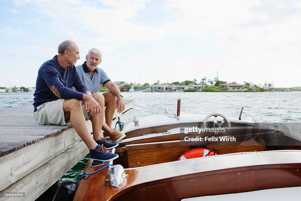 Two senior friends resting on jetty with moored motorboat