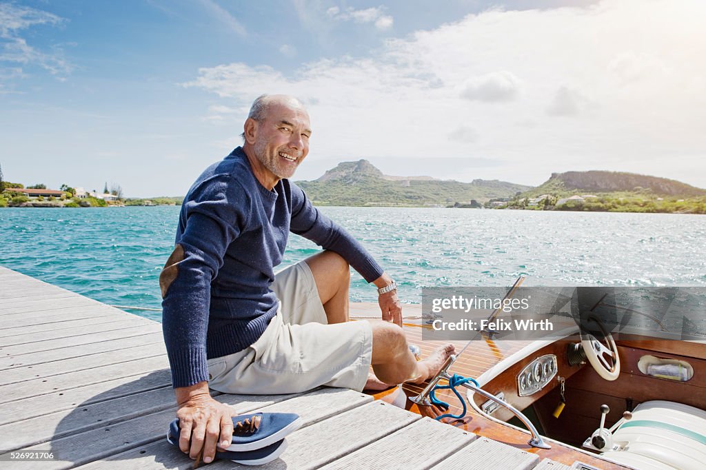 Senior man sitting on jetty with moored motorboat