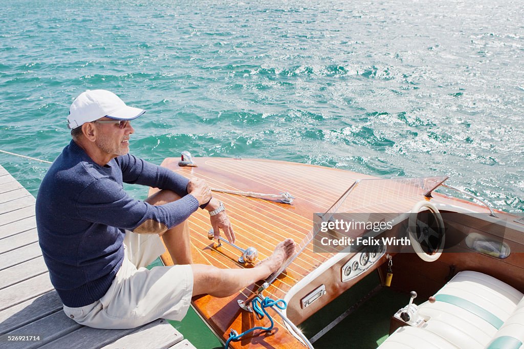 Senior man sitting on jetty with moored motorboat