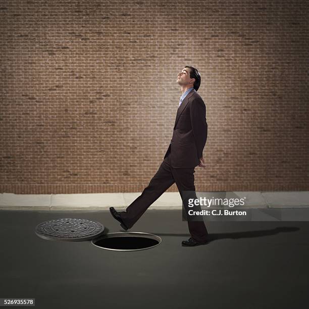 businessman walking over manhole - fato foto e immagini stock
