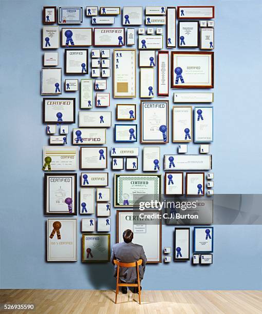 businessman staring at certificates on wall - obsessive stockfoto's en -beelden