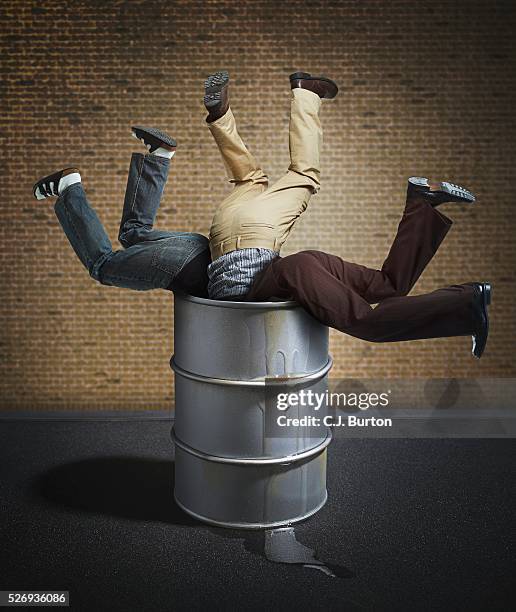 legs of three men sticking out of barrel - sinnlosigkeit stock-fotos und bilder