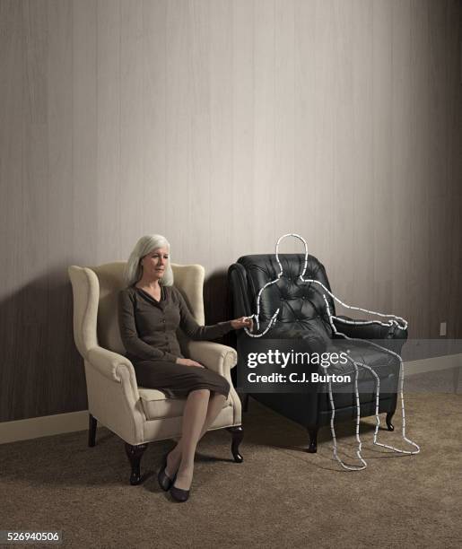 woman sitting in chair holding hand of outlined male shape - viuda fotografías e imágenes de stock