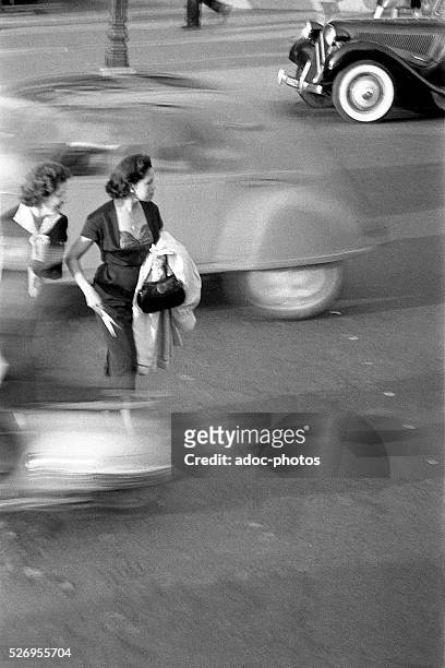Women crossing a street in the middle of traffic in Paris . In 1955.