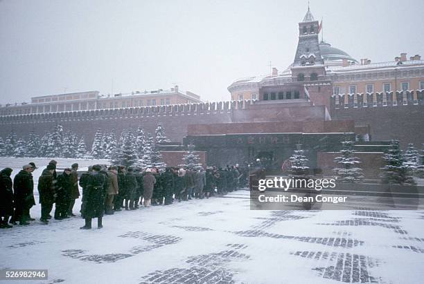 Snow falls upon a line of Russian citizens as they file slowly into the Lenin Mausoleum in Red Square. The building houses the preserved body of the...