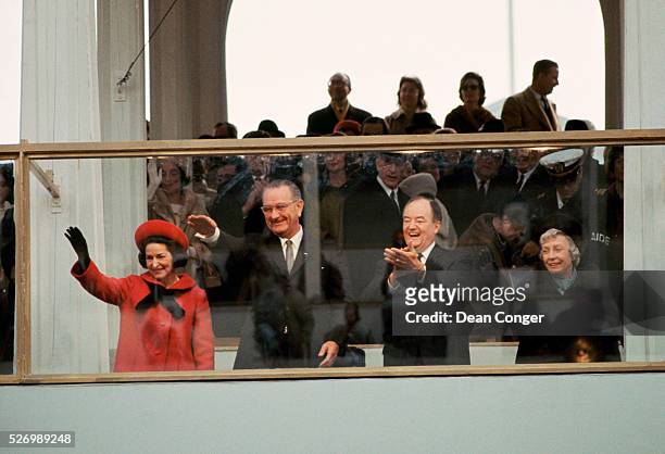 Lady Bird Johnson , President Lyndon Johnson , Vice President Hubert Humphrey and Mrs. Humphrey wave and clap as they watch the inaugural parade from...