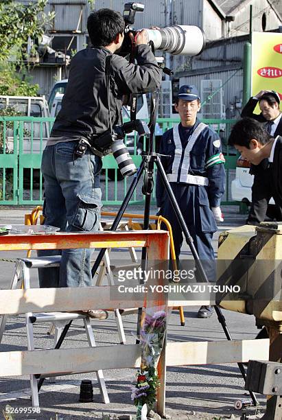 Press photographer takes pictures before a policeman standing guard while flower bouquets are placed near the train crashed site at Amagasaki city...