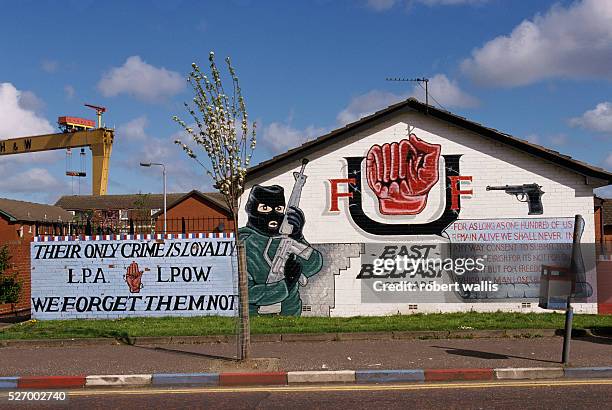 Unionist mural of a loyalist soldier wearing a black ski mask and holding a machine gun. The mural's memorial reads, "Their only crime is loyalty -...