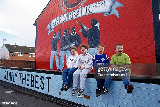 Four boys sitting beneath a unionist mural showing four masked unionist fighters in Belfast. The Northern Ireland peace talks have inspired many...