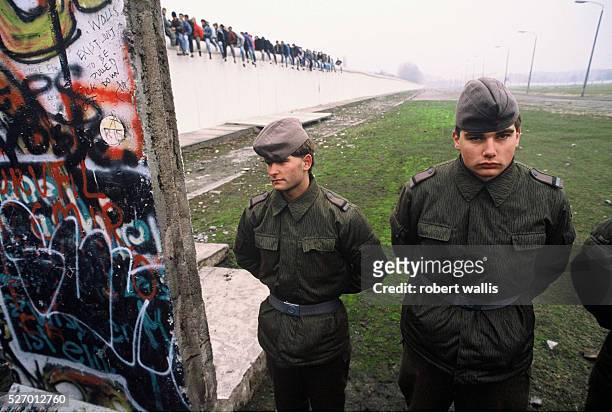 East German Border Guards look on in glumly at a newly opened section of the Berlin Wall a few days after the opening of the Wall on November 9,...