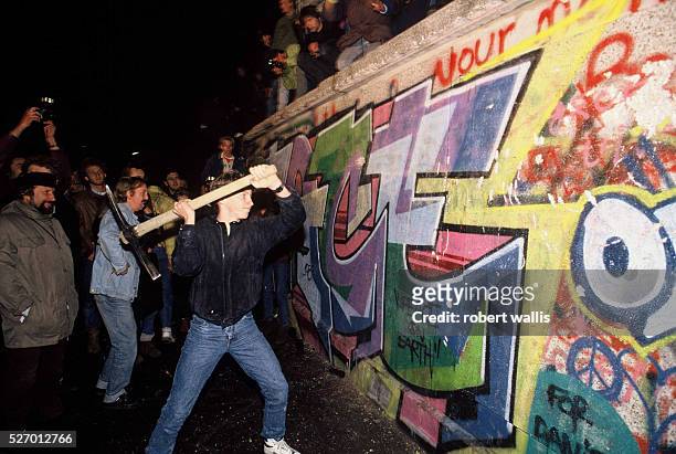 Man attacks the Berlin Wall with a pickaxe on the night of November 9th, 1989 as news spread rapidly that the East German Government would now start...